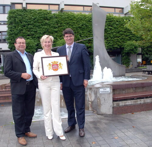 Foto: Bürgermeister Hans-Peter Haupt mit Sonja Schneider und Halil Bahadir von Monarchis vor dem Rathausbrunnen