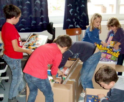 Grundschulkinder packen die Spiele für das neue Spielezimmer aus.