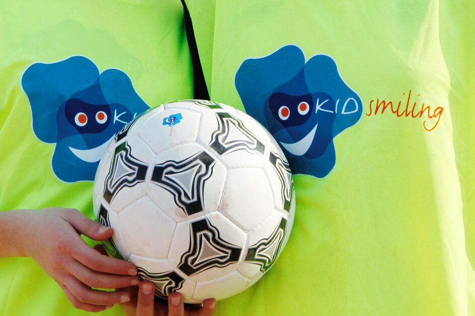 Zwei Kinder tragen Trikot mit Aufdruck KIDsmiling und halten einen Fußball